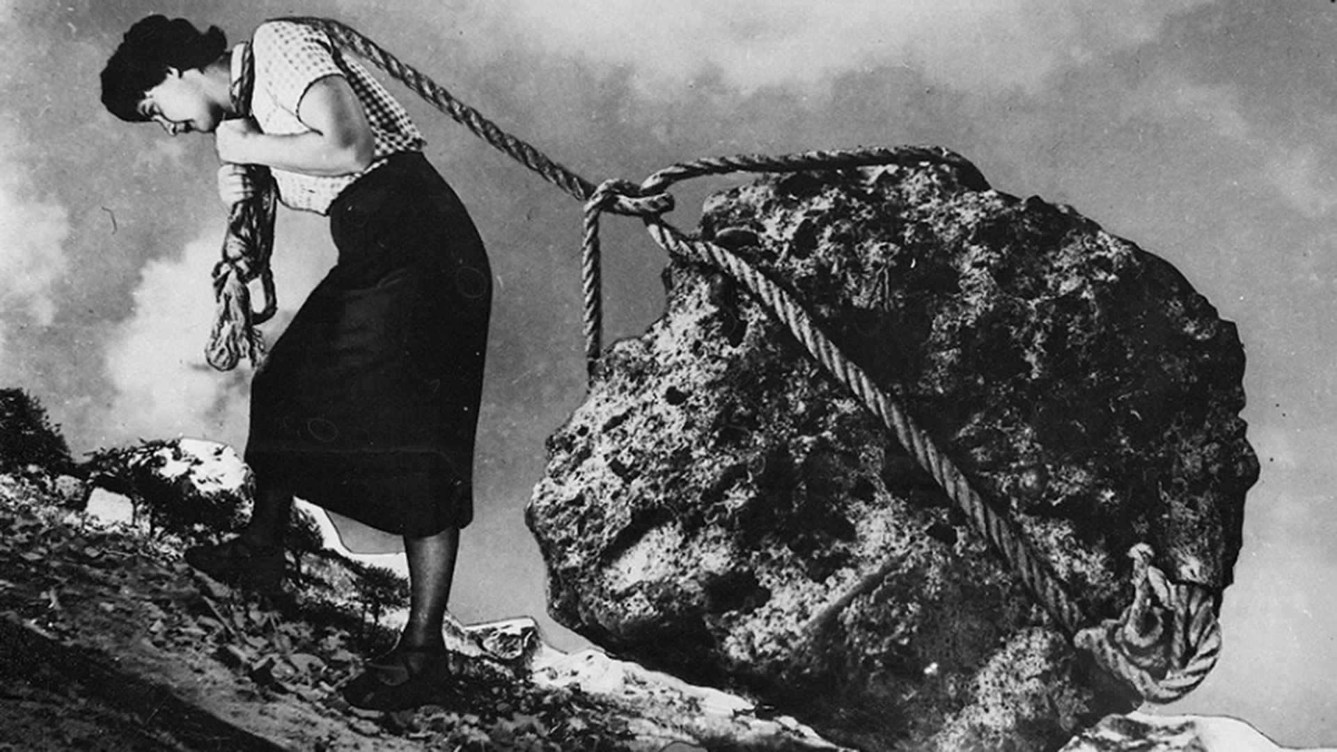 A woman hauling a large bolder wrapped in rope up a hill